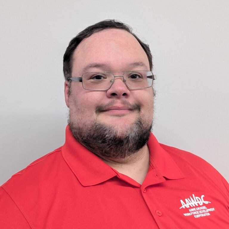 Person smiling in a red collared shirt with a logo, standing against a plain light gray background.