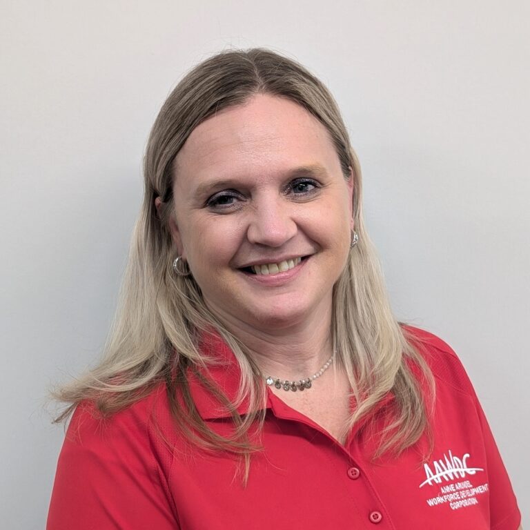 Person smiling in a red collared shirt with a logo, standing against a plain light gray background.