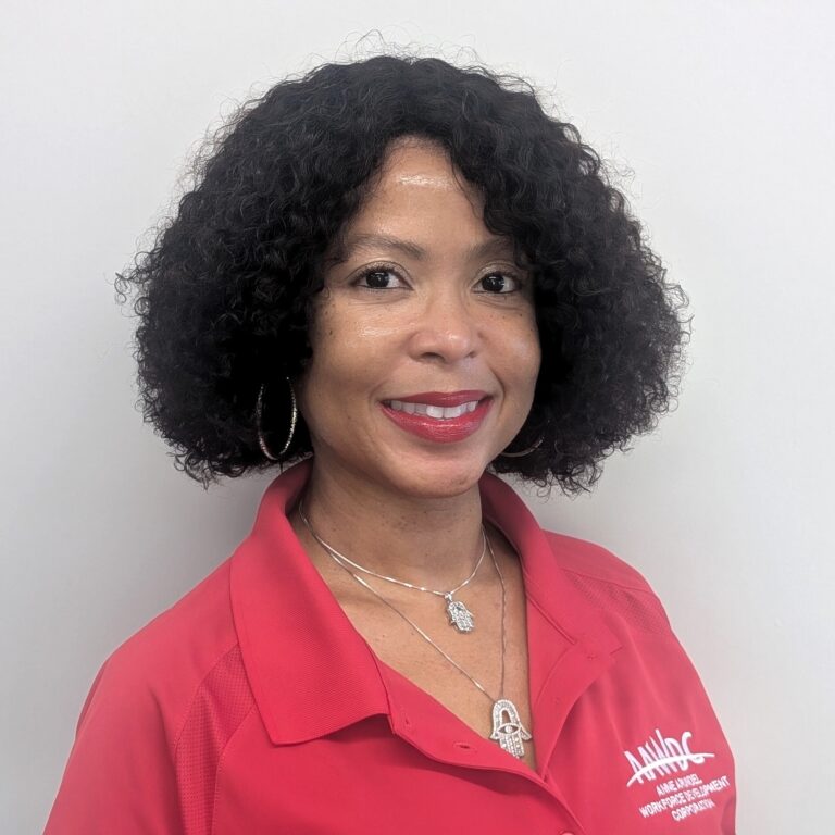 Person smiling in a red collared shirt with a logo, standing against a plain light gray background.