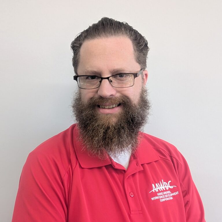 Person smiling in a red collared shirt with a logo, standing against a plain light gray background.