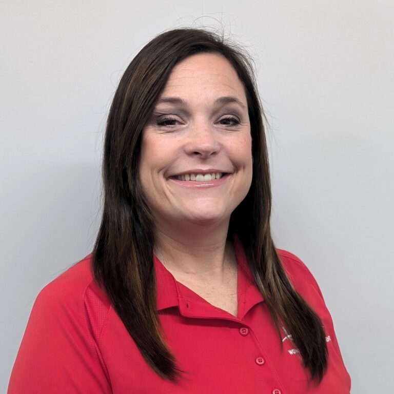 Person smiling in a red collared shirt, standing against a plain light gray background.