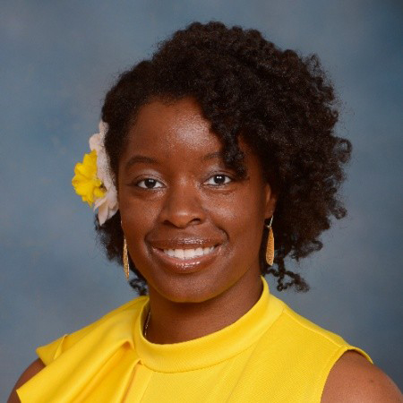Person smiling in a yellow top with a flower in their hair against a blue background.