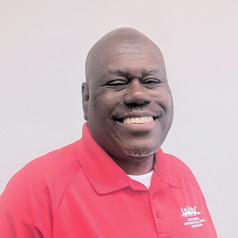 Person smiling in a red collared shirt with a logo, standing against a plain light gray background.