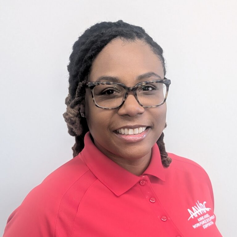 Person smiling in a red collared shirt with a logo, standing against a plain light gray background.