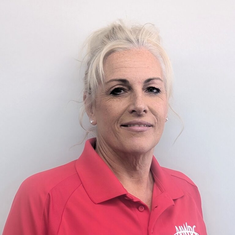 Person smiling in a red collared shirt with a logo, standing against a plain light gray background.