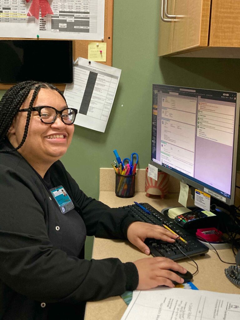 Person smiling while working at a desk on a computer in an office setting.