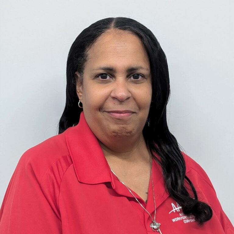 Person smiling in a red collared shirt with a logo, standing against a plain light gray background.