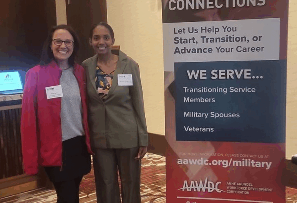 Two women smiling and standing next to a banner promoting career support for service members, military spouses, and veterans.