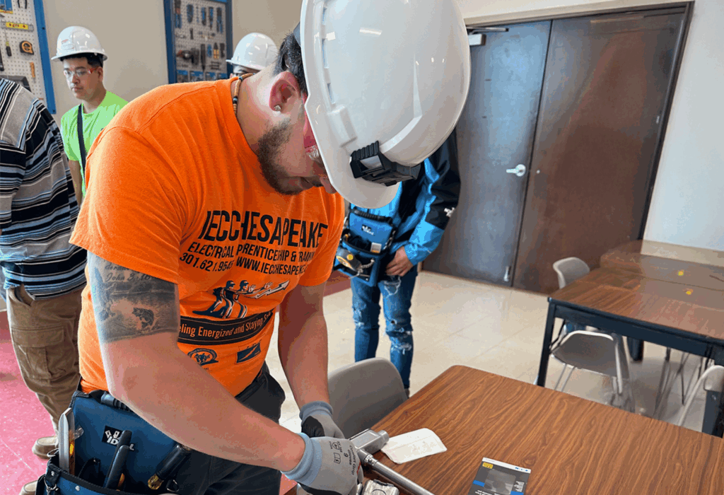 Person wearing a hard hat and safety gear working on an electrical training exercise in a classroom setting.