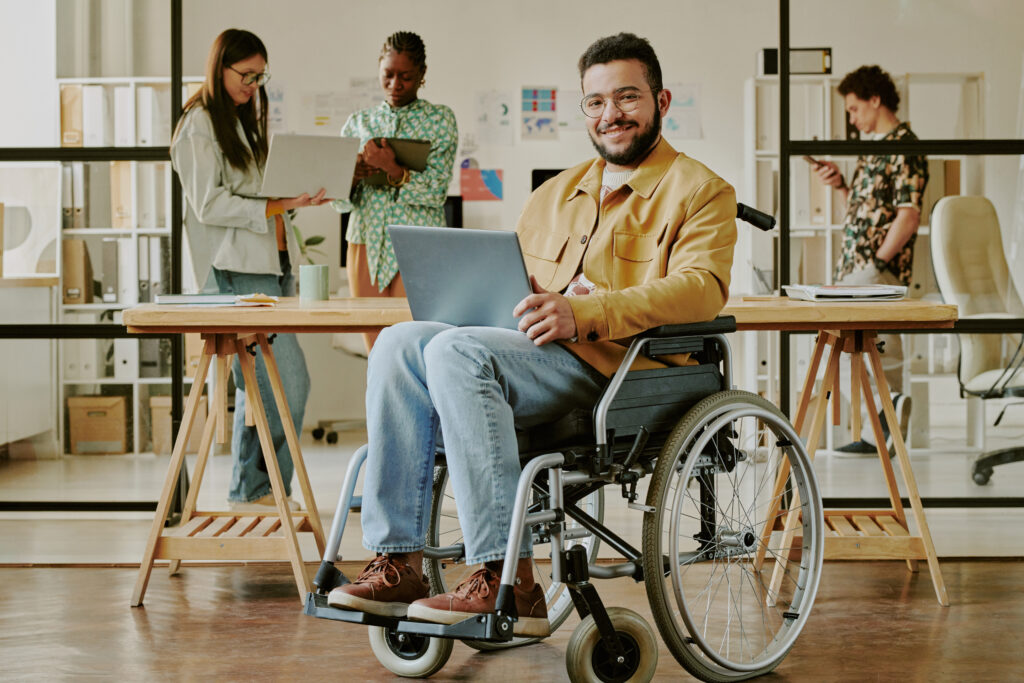 Young adult programmer with laptop smiling at camera while posing for portrait in office