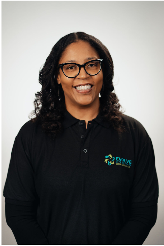 Person smiling and wearing glasses and a black shirt with the Evolve Life Centers logo.